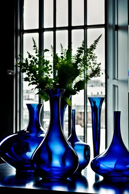 45 DEGREES LOW VIEW OF SIX BLUE COBALT GLASS VASES OF DIFFERENT SHAPES AND HEIGHTS RANDOMLY PLACED, VERY CLOSE TO EACH OTHERS, ON TOP OF A BLACK REFLEXIVE MARBLE TABLE, AGAINST A BRIGHTLY ILUMINATED WINDOW BACKGROUND