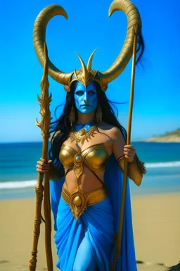 A picture of a blue faced Indian goddess with skin painted blue, blue body, wild black hair, stag horn antlers, elven ears, golden skirt, holding a staff on a sunny beach