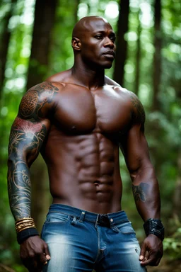 Alimi Ballard as muscular man bald with tribal tattoos wearing jeans and a teeshirt in a forest