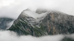 a massive sheer snowy mountain cliff with very sparse vegetationscaling vertically into the sky, partially obscured by dense clouds and mist. the borders — top, bottom, left, and right — fade smoothly into thick fog, while the center reveals the steep, rocky cliff face with fine texture and detail. atmospheric lighting, cinematic composition, natural colors, high contrast between fog and stone.