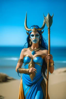 A picture of a beautiful blue faced indian goddess with skin painted blue, blue painted body, blue painted torso, wild black hair, stag antlers, elven ears, golden skirt, holding a staff on a sunny beach