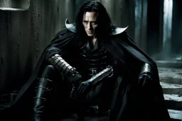 Action shot of Tom Hiddleston as Alucard from the live action "Hellsing" movie based on the anime of the same name. He is sitting, arms chained to a dungeon wall. He appears to be corpse wearing black wrappings that cover all except his head, feet, and hands. His straight, black hair hangs to the floor. A vague smile is on his gaunt face.