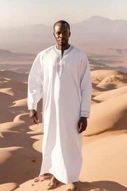 african man wearing white thobe. standing on high mountain looking out to the desert