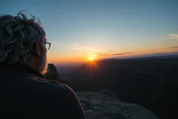 a large man with grey hair views sunset from a cliff