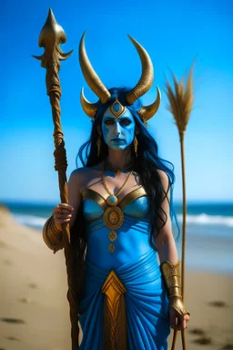 A picture of a blue faced Indian goddess with skin painted blue, blue body, wild black hair, stag horn antlers, elven ears, golden skirt, holding a staff on a sunny beach