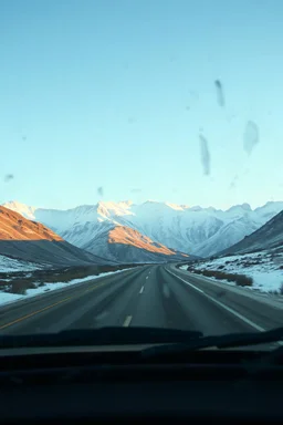 surreal mountain road seen through a dirty truck front window, dirty golden snow and wind