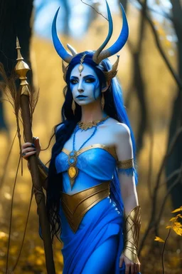 A picture of a beautiful blue faced Indian goddess with skin painted blue, blue body, blue torso, wild black hair, stag antlers, elven ears, golden skirt, holding a staff in a sunny forrest