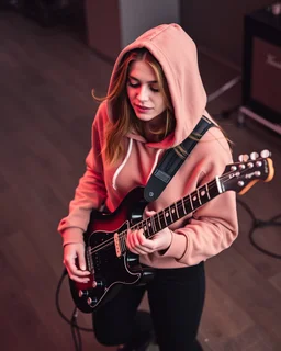 attractive woman wearing a hoodie and playing an electric guitar at high angle