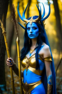 A picture of a beautiful blue faced indian goddess with skin painted blue, blue painted body, blue painted torso, wild black hair, stag antlers, elven ears, golden skirt, holding a staff in a sunny forrest