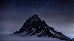 looking up at the tallest single mountain sharp face rising out of the misty foreground into the clear night sky background.