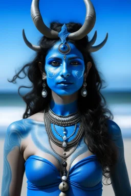 A photo of a blue skin Hindu goddess with painted blue face and body skin, wavy black hair deer antlers standing on a sunny beach