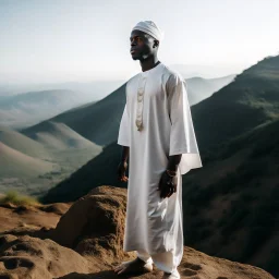 African man in white thobe, standing on top of mountain