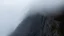 Placeholder: a scaling sheer mountain cliff obscured by clouds and fog. the the borders, top bottom, left and right are fog, while the center is sheer cliff.