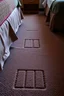 Placeholder: cheap motel room floor, square bed leg imprints in carpet, showing that furniture had been moved