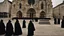 Placeholder: hooded monks in black robes in front of cathedral