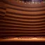 Placeholder: a close up view from stage of a single chair on stage under spotlight at a dark and empty symphony hall