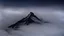 Placeholder: looking down at misty foreground and night sky background, no sun, single sharp narrow mountain peak coming through the mist in the center