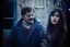 Placeholder: a young man and a beautiful woman standing next to each other, 1 9 8 0 s analog video, with mustache, small glasses, cold scene, out of focus background, house on background, the woman has long dark hair, photo realistic