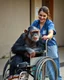 Placeholder: An old chimpanzee sitting on a wheel chair, beautiful nurse pushing his chair with smile