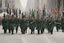 Placeholder: Soldiers marching in formation; military parade; marching along a street; green uniforms; medals and insignia; Rifles in their hands;