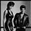 Placeholder: An extremely muscular young man who resembles Elvis Presley with pixie-cut black hair, wearing a black leather jacket and pants, standing next to a beautiful woman with auburn hair who resembles Raquel Welch, wearing a black two-piece bathing suit with a perfect shaped, stacked body, and a perfect face, 4k, 8k, 32k UHD, Hyper realistic, extremely colorful, vibrant, photorealistic, realistic, sharp, highly detailed, professional quality, beautiful, awesome, majestic,