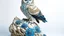 Placeholder: an owl perched on a white rock. The owl is facing towards the right side is turned slightly to the left. It has large, round, blue eyes that are piercing and appear to be looking directly at the viewer. Its body is covered in intricate patterns and feathers, giving it a realistic appearance. The background is a light blue color, making the owl stand out even more. The rock it is perched on is also white and appears to be made of snow or ice. The overall mood is peaceful and serene.