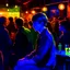 Placeholder: a single figure in a crowded bar at night, young people, dark colors, impressionist style