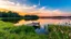 Placeholder: A tranquil lakeside scene at sunrise. The calm water reflects the colors of the sky, and a small wooden dock extends into the lake. Surrounding the lake are lush, green trees and soft grasses and flowers swaying gently in the breeze. Award-winning photograph, beautiful composition, exquisite detail and illumination