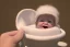 Placeholder:  baby Who looks like donald trump in a Baby carriage tucked in wearing a bonnet and sucking his thumb