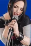 Placeholder: attractive female country music singer leaning forward while holding microphone in one hand, other hand brought up to side of neck, change clothing to plaid in natural tones, leather bracelets on wrists, long hair, mouth open singing, rings on fingers, eyes closed