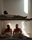 Placeholder: full figure shot photography of two arab prisoners in cell sitting on the edge of a bed talking, muscular hairy chubby 45 years old,long beard, low lights, misery and poverty, in undershirt and boxers, little light enters from a skylight above, lights from above, photorealistic, ambient occlusion, front view from below