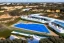 Placeholder: Sunset algarve in quinta do lago, one straight line building of 250 meters long modern luxury architecture with pool on rooftop, with green roofs and sun loungers next to pool, on the left side overlooking a tennis and padel sport facility and inserted in the Ria Formosa Natural park, on a slope with pinus pinea, a wrap around low speed veicular road