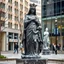 Placeholder: photo of a lady statue made of black marbel showing a goddoss love mother and baby in a modern city center