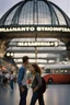 Placeholder: A realistic photo of a Milano in main station in the background, a pair of inamorato young people on the street, typically Italian, late summer evening. Photo taken by Mamiya M645 camera with low-speed film, highly detailed, wide lens.