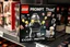 Placeholder: darkly satirical LEGO box titled "PROMPT Thief" on a store shelf. Box image features a dystopian overweight AI troll minifigure, clutching stolen ideas in the form of tiny pixelated idea lego bricks shaped as lightbulbs. background is a bleak digital void with fragments of vogue magazine covers floating in the abyss. A defeated brain-headed minifigure artist slumps in the corner clutching a lego made laptop, tagline on box reads "COPY, PASTE, STEAL"