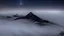 Placeholder: looking down at misty foreground and night sky background, no sun, single sharp narrow mountain peak coming through the mist in the center