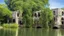 Placeholder: A ruined stone building in a lake, balconies, verandas, arches, bridges, spires, stairs, trees, dense foliage, spanish moss, ivy, blue sky, white clouds