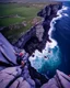 Placeholder: from the point of view of a rock climber, look down at the ocean rocks below as you climb high into the bluffs of ireland. holding on to the cliff face, the ocean below storms and swirls around a giant whirlpool, a great pit in the ocean