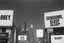 Placeholder: greyscale cityscape; large white billboards populate the city with black block lettering with text "OBEY", "REPRODUCE", "CONSUME", "BUY", "SLEEP", 'They Live' by john_carpenter movie still, concept art