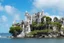 Placeholder: A futuristic ruined gothic building on an island floating over the sea with balconies, verandas, many arches, bridges, spires, paths, trees, dense foliage, spanish moss, ivy, blue sky, white clouds