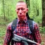 Placeholder: Georges st pierre with a red plaid shirt, a backpack and a gun in the forest infested by zombies