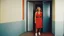 Placeholder: [color photo by Russ Meyer, in the 90ties] facing a lonely smiling woman on the door step of an appartement, in gym, talking. we see the corridor behind her