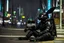 Placeholder: Half robot, half organic black rabbit wearing body armor. He is sittin on the neon-soaked sidewalks of the city. Photograph.