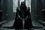 Placeholder: Action shot of Tom Hiddleston as Alucard from the live action "Hellsing" movie based on the anime of the same name. He is sitting, arms chained to a dungeon wall. He appears to be little more than a desiccated corpse wearing black wrappings that cover all except his head, feet, and hands. His straight, black hair hangs to the floor. A vague smile is on his gaunt face.