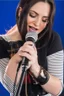 Placeholder: attractive female country music singer leaning forward while holding microphone in one hand, other hand brought up to side of neck, change clothing to plaid in natural tones, leather bracelets on wrists, long hair, mouth open singing, rings on fingers, eyes closed