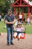 Placeholder: a 40 year old dad in the playground with his young 3 year old daughter playing on the swing but the dad is distracted by all the other kids curvy mums . there are many kids playing on the playground