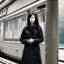 Placeholder: A young Asian woman with long hair and a black trench coat waiting for a woman at a train station in Paris