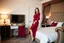 Placeholder: very beautiful sexy lady with beautful dark red midi skirt and blouse standing in a luxury bedroom with high heels next to makeup desk looking to camera