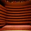 Placeholder: a single chair on stage in the beam of single spotlight facing empty audience at a dark and empty symphony hall