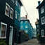 Placeholder: Fotografia di strada assurda e falsa a Magog blu weirdcore dai colori vivaci. Sfasato. Non luogo falso, inusuale. Max Ernst. Le case sono false e dipinte di nero chiaro con cose stilizzate e dettagli. Ci sono finestrelle false quadrate, che danno un senso distopico e molto surreale, disposte in modo casuale. L'atmosfera generale sembra noiosa e onirica, con un contrasto tra elementi reali ed elementi dipinti falsi, René Magritte